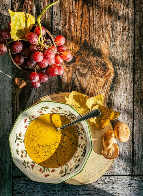 Vista dall'alto di un piatto con zuppa di zucca grappolo d'uva decorare l'immagine Sfondo in legno