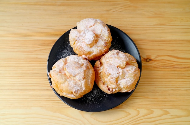 Vista dall'alto di un piatto di pasticcini francesi Choux a la Creme con zucchero a velo servito su un tavolo di legno