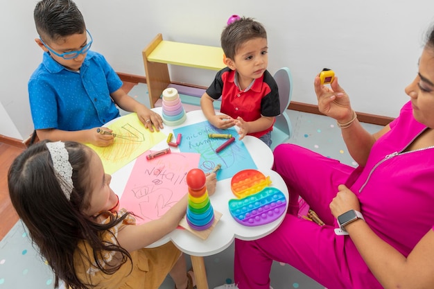 Vista dall'alto di un tavolo con bambini e un medico pediatra che disegna su fogli a colori con i pastelli