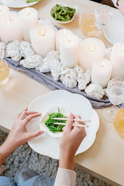 Vista dall'alto di un tavolo con candele e una persona che usa le bacchette per mangiare verdure verdi