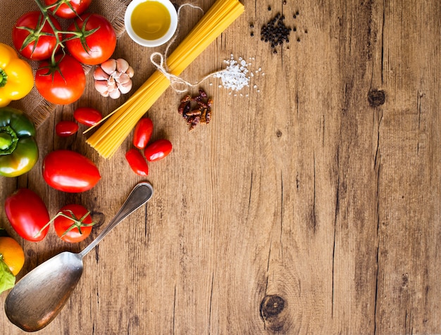 Vista dall'alto di un tavolo di legno pieno di pasta italiana ingradients come peperoni pomodori olio d'oliva basi