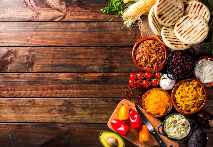Foto vista dall'alto di un tavolo rustico in legno con diversi ingredienti per cucinare e riempire le arepas