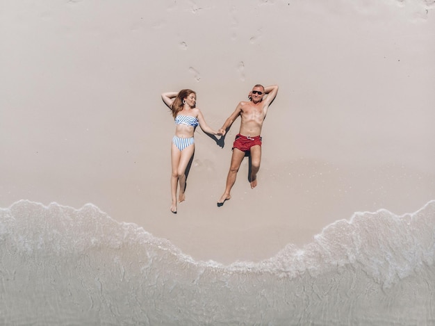 Vista dall'alto di una bella coppia adorabile in costume da bagno sdraiata sulla sabbia calda della spiaggia e prendere il sole, tenendosi per mano sotto i raggi del sole cocente. concetto di romanticismo.