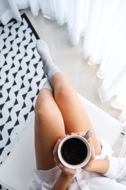 Vista dall'alto di una bella donna che beve il caffè caldo in camera da letto a casa la mattina