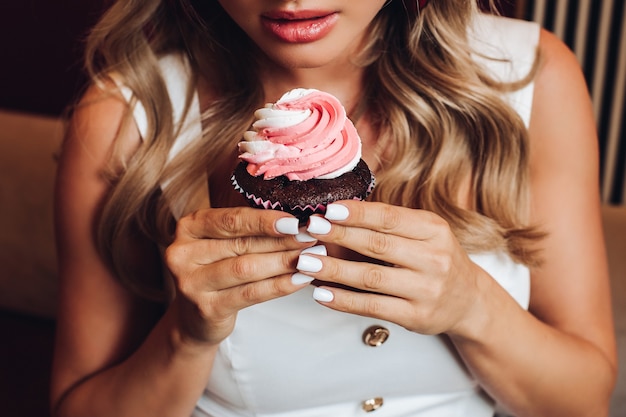 Vista dall'alto di una bella ragazza che tiene in mano un delizioso cupcake rosa. Giovane femmina guardando gustosa torta al cioccolato dolce e godendo l'odore. Concetto di pasticceria e dessert.