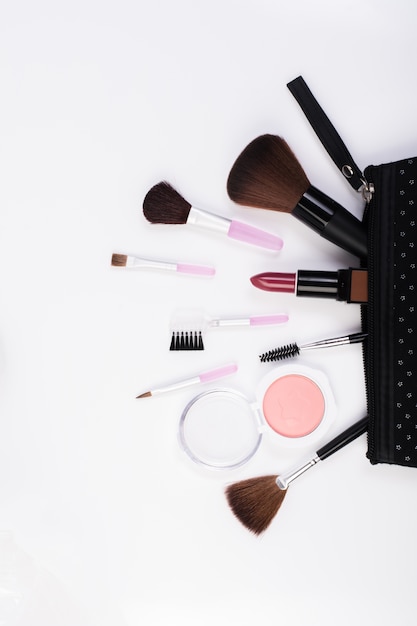 Vista dall&#39;alto di una borsa da make up, con prodotti cosmetici estetici che si sfilano su uno sfondo bianco.