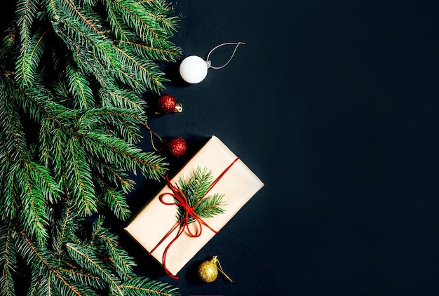 Vista dall'alto di una confezione regalo, rami di un albero di natale, decorazioni natalizie su sfondo nero