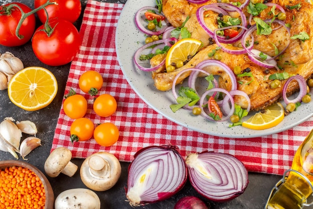 Vista dall'alto di una deliziosa cena piatto di pollo fritto con varie spezie e cibi pomodori con steli lenticchie rosse aglio bottiglia di olio caduto funghi al limone su sfondo di colore scuro