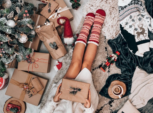 Vista dall'alto di una donna che tiene una confezione regalo marrone su un tappeto accanto a un albero di Natale