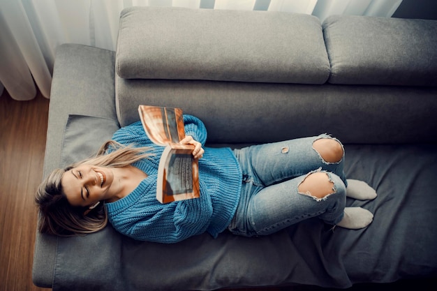 Vista dall'alto di una donna felice che legge un libro interessante nella sua casa confortevole