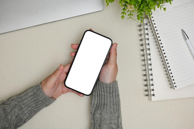 Vista dall'alto di una donna in un comodo maglione grigio che utilizza il suo smartphone alla sua scrivania minima