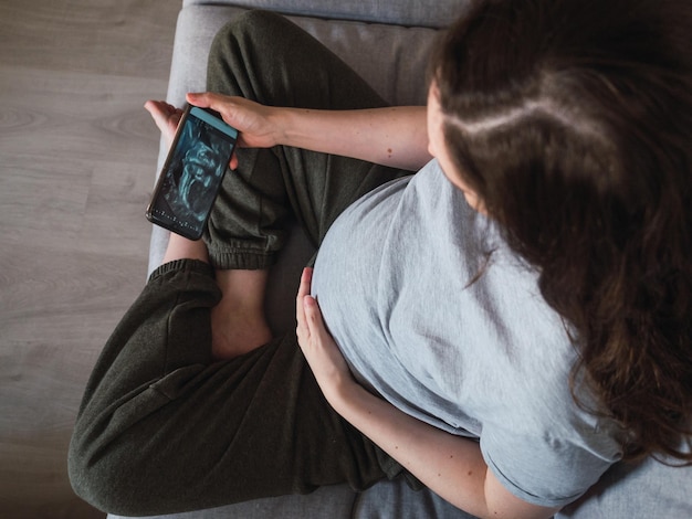 Vista dall'alto di una donna incinta che guarda la scansione a ultrasuoni del suo bambino sul suo smartphonexA