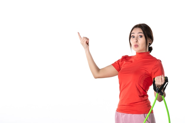 Vista dall'alto di una giovane donna che raccoglie ordinatamente i suoi capelli vestiti con una camicetta redorange e che tiene l'accessorio sportivo in corda rivolto verso l'alto su sfondo bianco