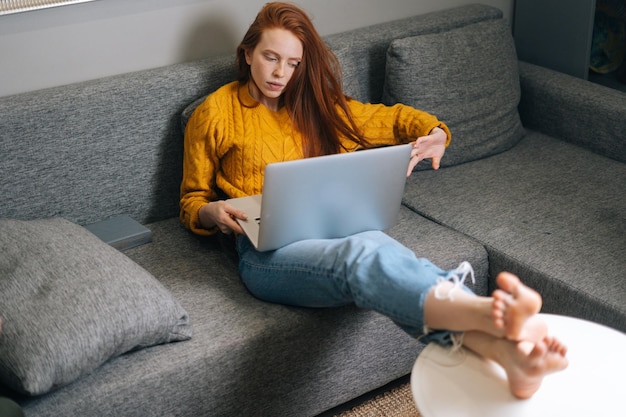 Vista dall'alto di una giovane donna d'affari esausta che digita sul computer portatile seduto sul divano in soggiorno Libera professionista femminile oberata di lavoro che lavora chattando in internet dal computer