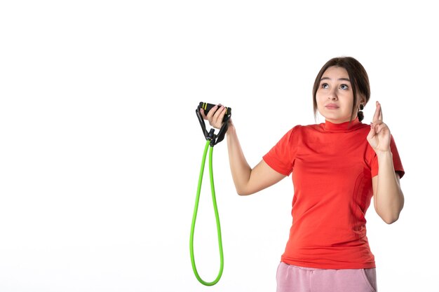 Vista dall'alto di una giovane donna piena di speranza che raccoglie ordinatamente i suoi capelli vestiti con una camicetta redorange e che tiene l'accessorio sportivo in corda su sfondo bianco