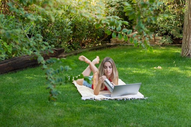 Vista dall'alto di una giovane donna sdraiata in giardino che lavora come libera professionista per la propria attività online