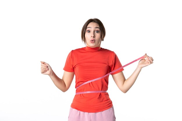 Vista dall'alto di una giovane donna sorpresa con una camicetta rossoarancio e un misuratore che misura la sua vita su sfondo bianco