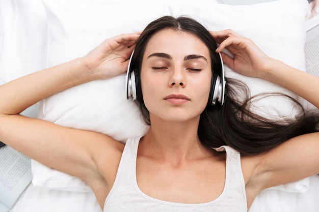 Vista dall'alto di una giovane e bella donna che ascolta la musica con le cuffie mentre giaceva a letto