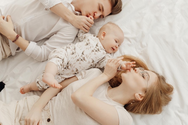 Vista dall'alto di una giovane famiglia idilliaca felice in abiti bianchi con un neonato sorridente e paffuto dagli occhi azzurri