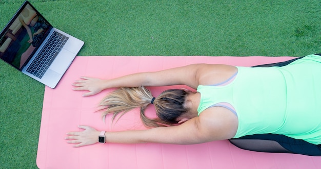 Vista dall'alto di una giovane ragazza che fa una lezione di yoga online nel giardino di casa sua