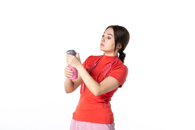 Vista dall'alto di una giovane ragazza focalizzata in camicetta rossa che tiene in mano un misuratore e un termos su sfondo bianco