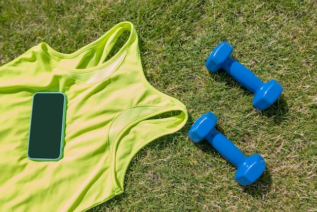 Vista dall'alto di una maglia sportiva con manubri e uno smartphone sull'erba di un campo da calcio