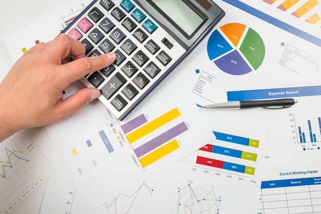 Vista dall'alto di una mano che digita su una calcolatrice sullo sfondo dei grafici Fogli di calcolo grafico sviluppo finanziario conti bancari statistiche economia analisi dei dati analisi degli investimenti borsa