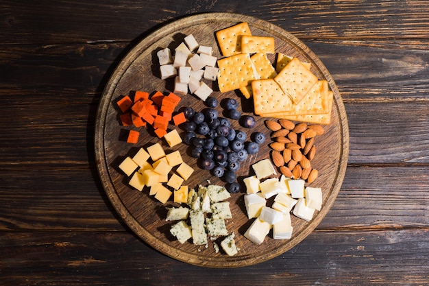 Vista dall'alto di uno spuntino di vario genere disposto in porzioni su un vassoio di legno Formaggi di vario genere con cracker di megdale e mirtilli