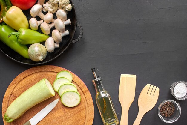 Vista dall'alto di verdure fresche per una sana alimentazione. Ci sono ingredienti per cucinare come cavolfiore, champignon, peperoni, pomodori, cipolle su un piatto. Bottiglia di olio d'oliva, cucina in legnow