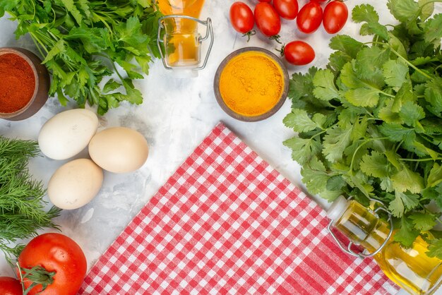 Vista dall'alto di verdure fresche zenzero giallo olio caduto bottiglia verde fasci pomodori con steli asciugamano rosso spogliato