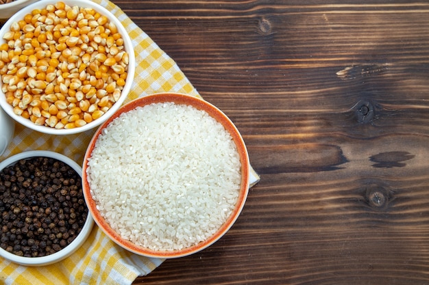 vista dall'alto diversi ingredienti grezzi riso mais lenticchie e grano saraceno in piastre su superficie marrone