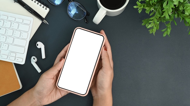 Vista dall'alto donna che tiene in mano uno smartphone con schermo bianco sulla scrivania dell'ufficio.