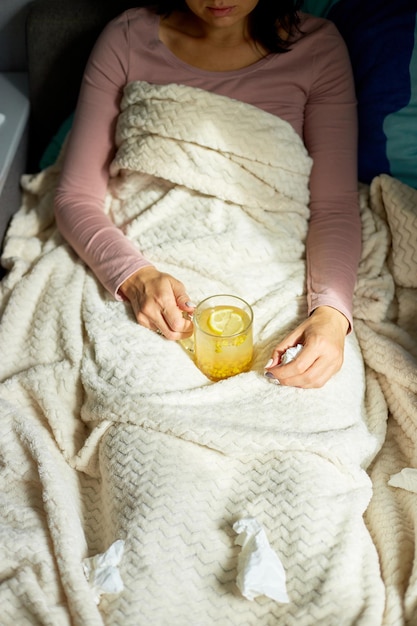 Vista dall'alto Donna malata che tiene una tazza di tè caldo all'olivello spinoso e seduta sotto la coperta a casa, signora malata, rimedi naturali per il raffreddore, concetto di medicina naturale.