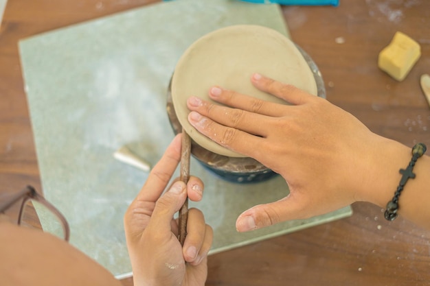 Vista dall'alto Donna vasaio che lavora al tornio del vasaio che fa vaso di ceramica dall'argilla nel laboratorio di ceramica Mano di messa a fuoco giovane donna che attacca la parte del prodotto in argilla al futuro prodotto in ceramica Laboratorio di ceramica