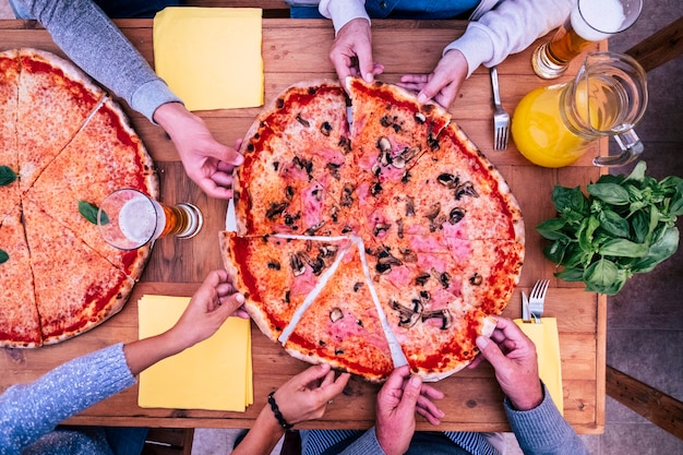 Vista dall'alto e dall'alto di due grandi pizze con molte mani che ne prendono un pezzo - tavolo di legno - cena in famiglia o tra amici