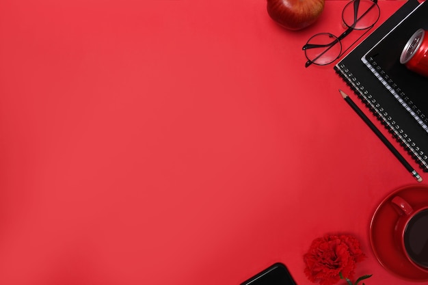 Vista dall'alto elegante posto di lavoro con taccuino, occhiali, tazza di caffè, telefono cellulare e penna su sfondo rosso.