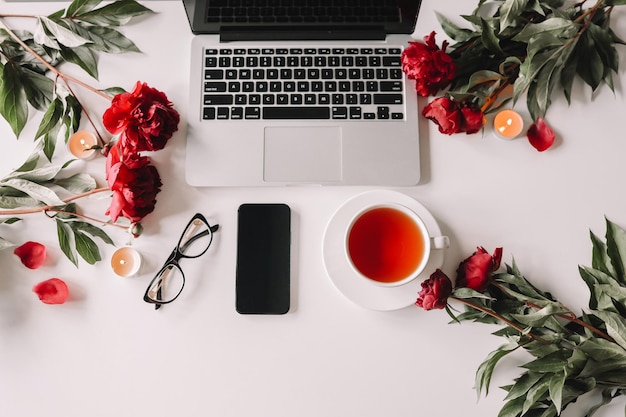 Vista dall'alto femminile sul posto di lavoro telefono portatile tazza di tè peonie occhiali