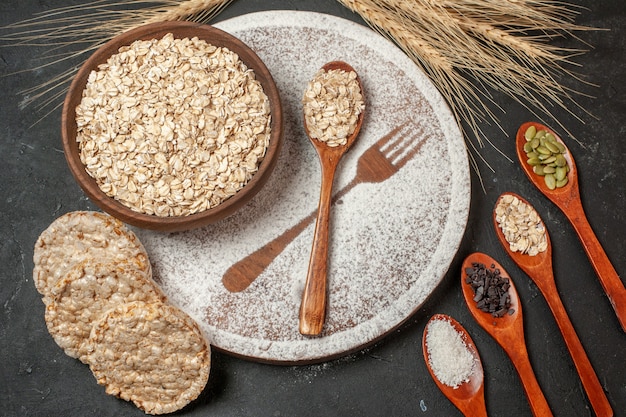 vista dall'alto fiocchi d'avena in ciotola di legno forchetta impronta con zucchero a velo cucchiaio di legno cracker di riso sul tavolo