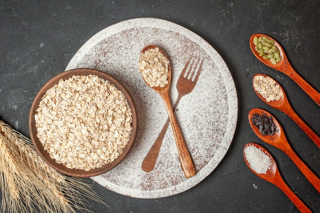 vista dall'alto fiocchi d'avena in ciotola di legno forchetta impronta con zucchero a velo cucchiaio di legno spighe di grano cucchiai di legno con altri animali sul tavolo