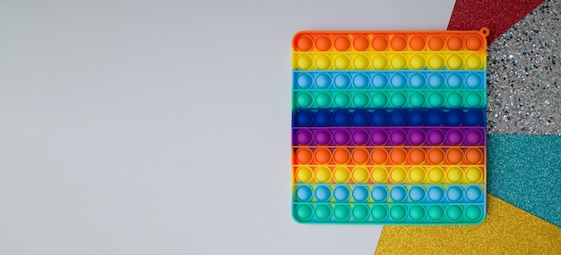 Vista dall'alto giocattolo in silicone arcobaleno antistress pop su sfondo colorato. Banner giocattolo push sensoriale giocattolo popolare per bambini