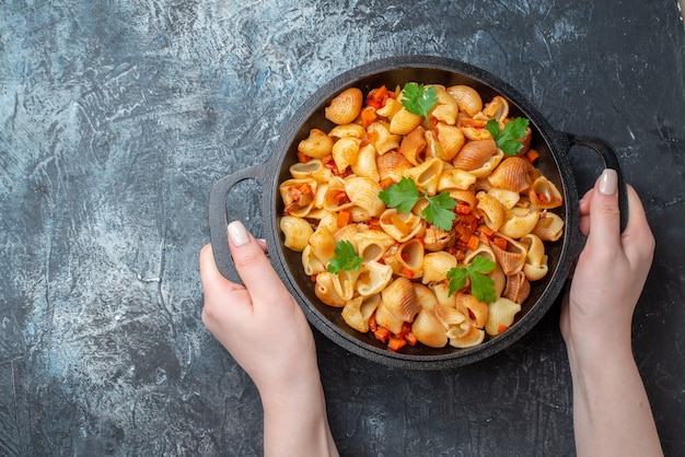 vista dall'alto gustosa pasta in padella nelle mani della donna su sfondo grigio