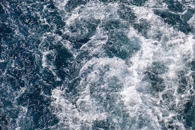 Vista dall'alto in basso della superficie dell'acqua di mare. La schiuma bianca ondeggia la struttura come sfondo naturale.