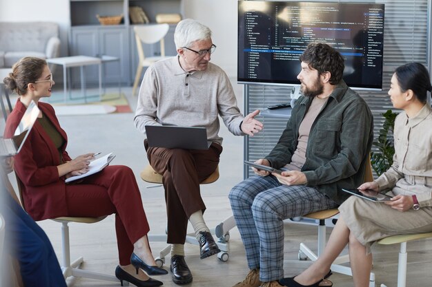 Vista dall'alto in un team aziendale contemporaneo e diversificato seduto in cerchio durante la riunione strategica, concentrarsi sull'uomo d'affari senior al centro