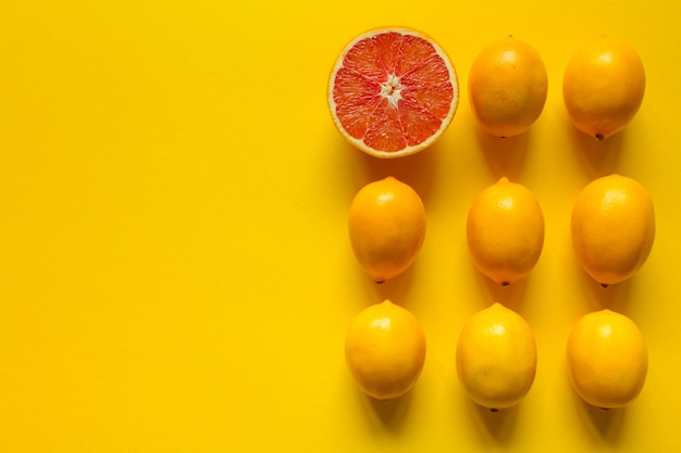 Vista dall'alto intero e fette di limone maturo e pompelmo disposti in più file su una superficie gialla, concetto di salute e vitamine