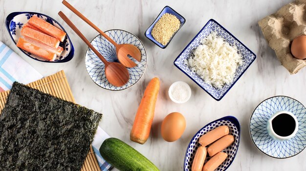 Vista dall'alto Kimbap/ingredienti di Gimbap/rotolo di riso coreano sul tavolo di marmo bianco. Laver/Nori, carota, riso, sale, semi di sesamo, cetriolo, polpa di granchio e salsiccia.