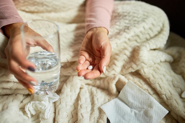 Vista dall'alto La donna malata tiene in mano la medicina, le pillole e il bicchiere d'acqua mentre si riprende a casa, donna malata che prende la pillola mentre è seduta sul divano a casa