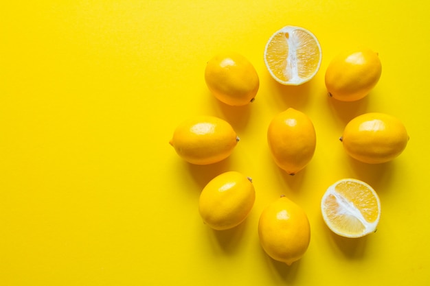 Vista dall'alto limoni maturi interi e affettati disposti a forma di quadrante su una superficie gialla