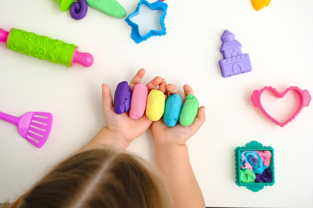 vista dall'alto mani dei bambini con plastilina colorata, pasta da gioco, stampi per modellare su sfondo bianco, concetto di giochi educativi domestici