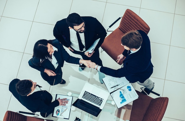 Vista dall'alto: partner commerciali affidabili della stretta di mano dopo la discussione del contratto finanziario in ufficio. La foto ha uno spazio vuoto per il testo.