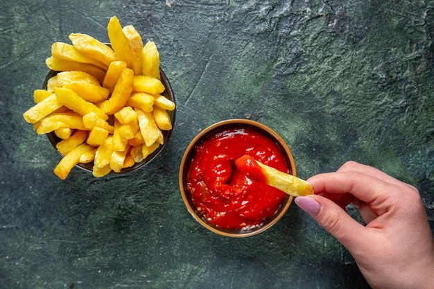 Vista dall'alto patatine fritte mangiare con ketchup da femmina su superficie scura